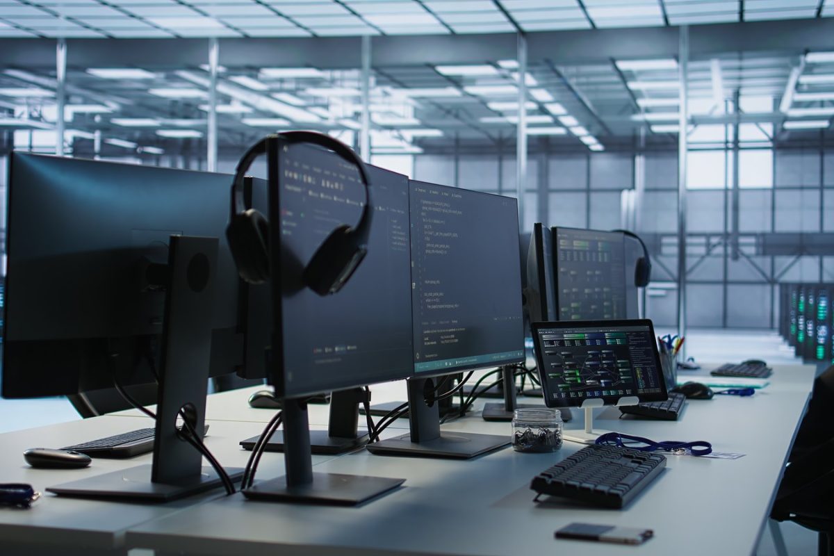 Postes de travail avec écrans de code et de supervision devant une salle de serveurs, illustration du monitoring d’AI Mode