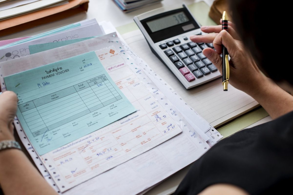 Pièces comptables et bons de paiement vérifiés à la calculatrice, illustration du contrôle fiscal d’une comptabilité externalisée