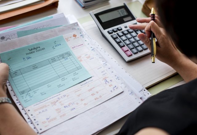 Pièces comptables et bons de paiement vérifiés à la calculatrice, illustration du contrôle fiscal d’une comptabilité externalisée