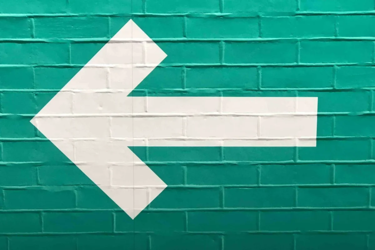Flèche blanche vers la gauche peinte sur un mur de briques vertes, symbole du bouton retour du navigateur