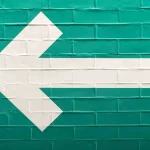 Flèche blanche vers la gauche peinte sur un mur de briques vertes, symbole du bouton retour du navigateur