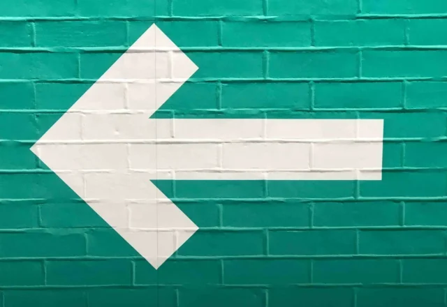 Flèche blanche vers la gauche peinte sur un mur de briques vertes, symbole du bouton retour du navigateur