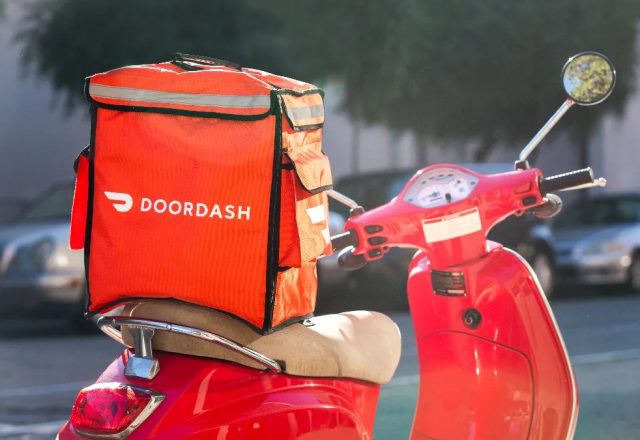 Sac de livraison DoorDash fixé à l’arrière d’un scooter rouge garé dans une rue