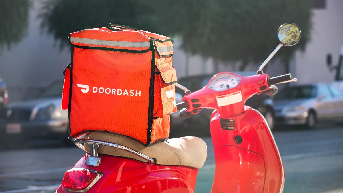 Sac de livraison DoorDash fixé à l’arrière d’un scooter rouge garé dans une rue