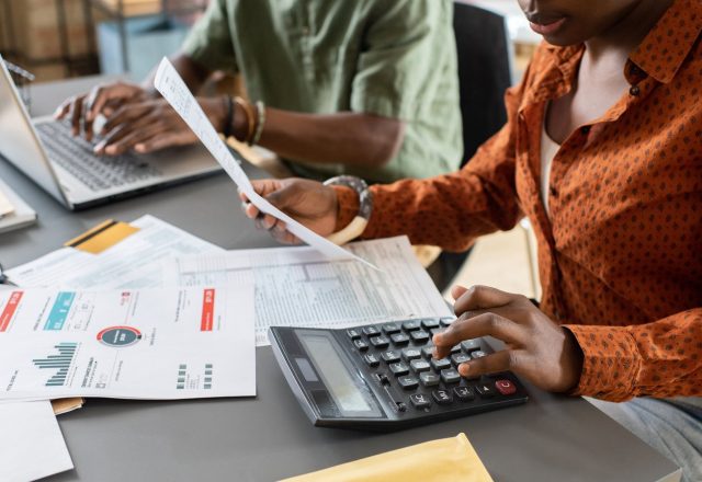 Deux collaborateurs d’une équipe comptable, l’une vérifiant une facture à la calculatrice, l’autre saisissant sur ordinateur portable