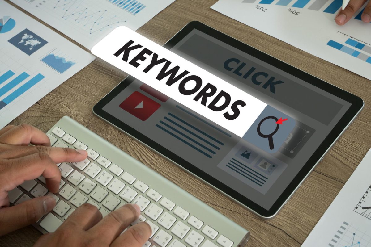 Tablette affichant le mot Keywords au-dessus d'une maquette de page web, à côté de graphiques imprimés