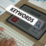 Tablette affichant le mot Keywords au-dessus d'une maquette de page web, à côté de graphiques imprimés