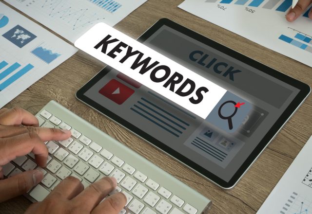 Tablette affichant le mot Keywords au-dessus d'une maquette de page web, à côté de graphiques imprimés