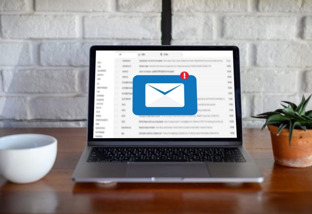 Ordinateur portable affichant une boîte de réception et une icône d’email avec notification, posé sur un bureau