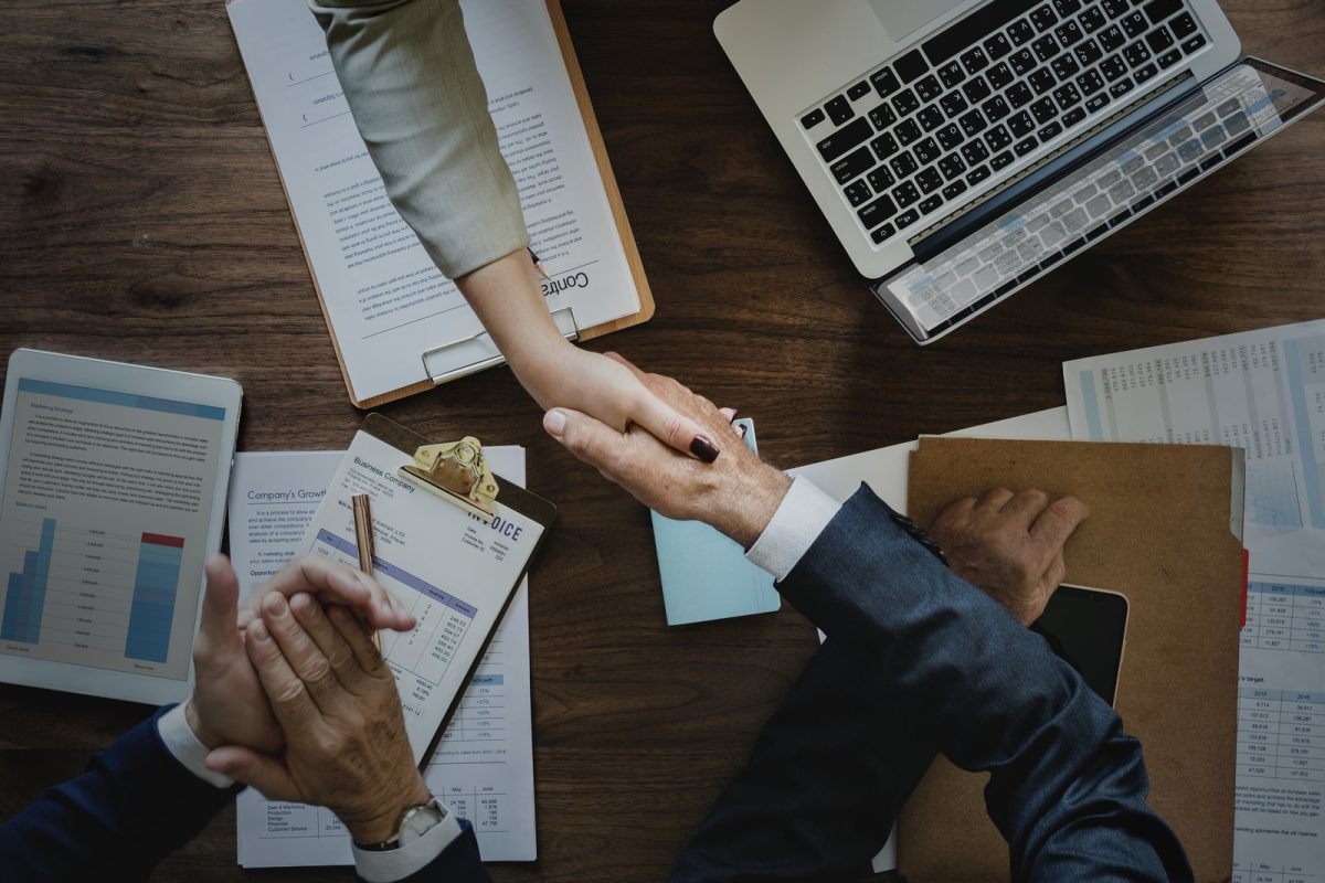 Poignée de main au-dessus d’un contrat, ordinateur portable et documents sur un bureau