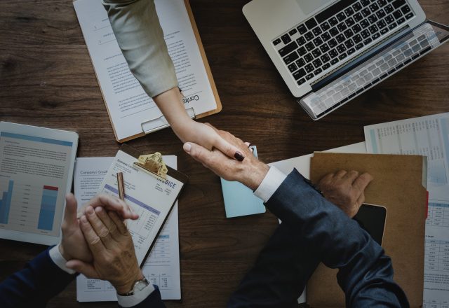 Poignée de main au-dessus d’un contrat, ordinateur portable et documents sur un bureau