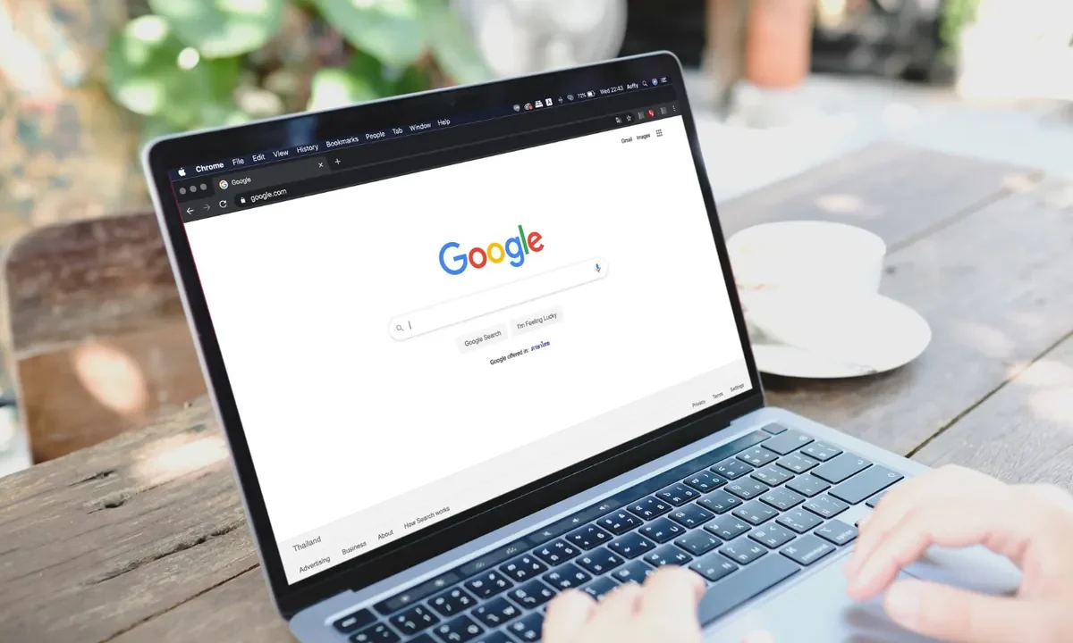 Personne tapant sur un ordinateur portable ouvert sur la page d’accueil de la recherche Google, en terrasse