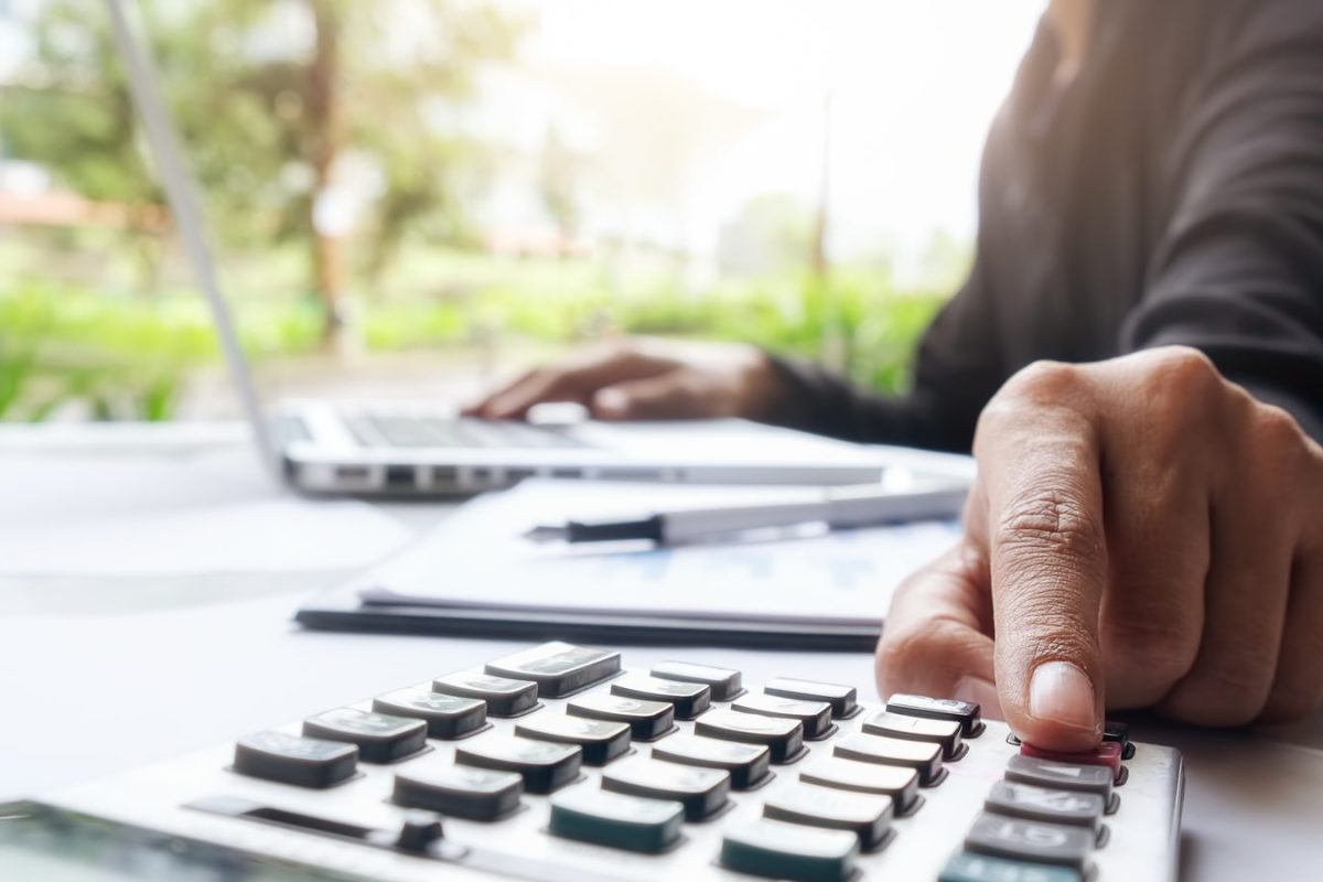 Main utilisant une calculatrice devant un ordinateur portable et des documents comptables
