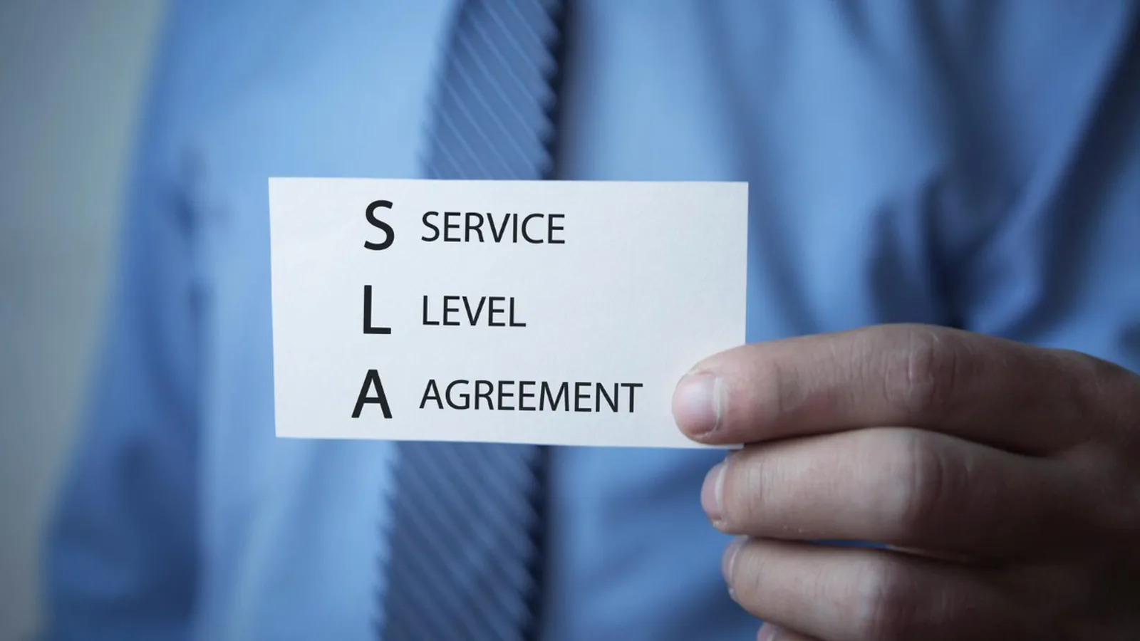 Carte de visite portant la mention Service Level Agreement tenue par une personne en chemise et cravate
