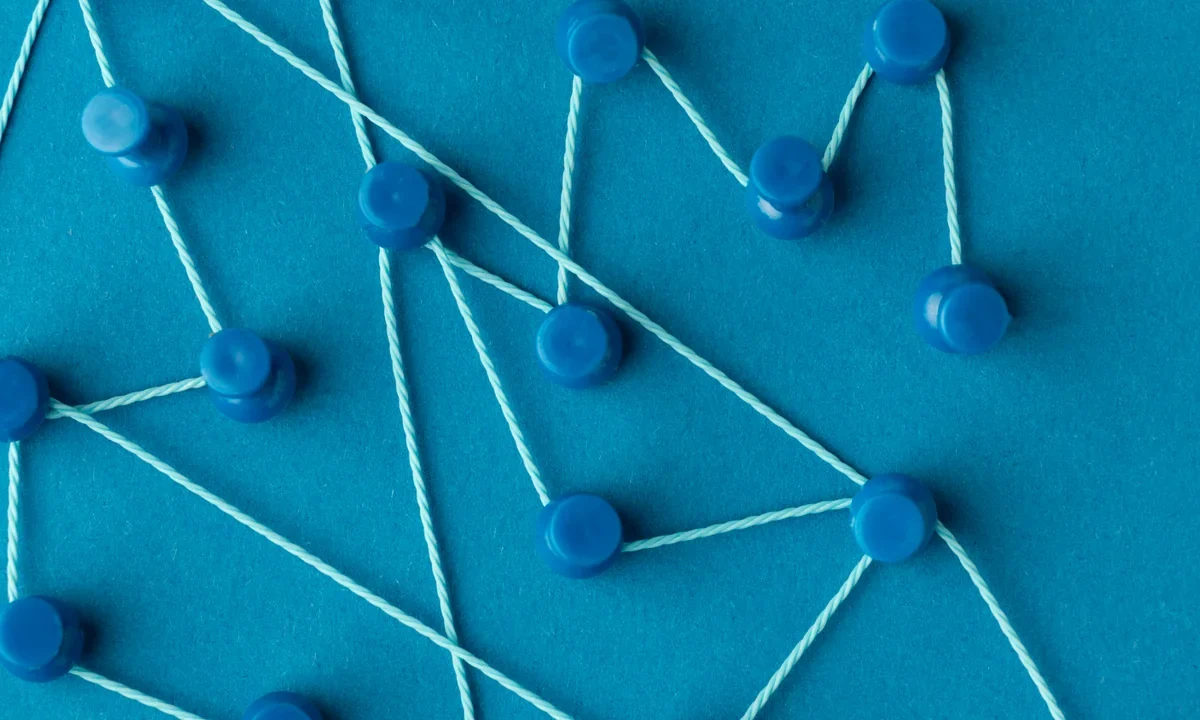 Punaises bleues reliées par des fils sur fond bleu, image d’un réseau de liens