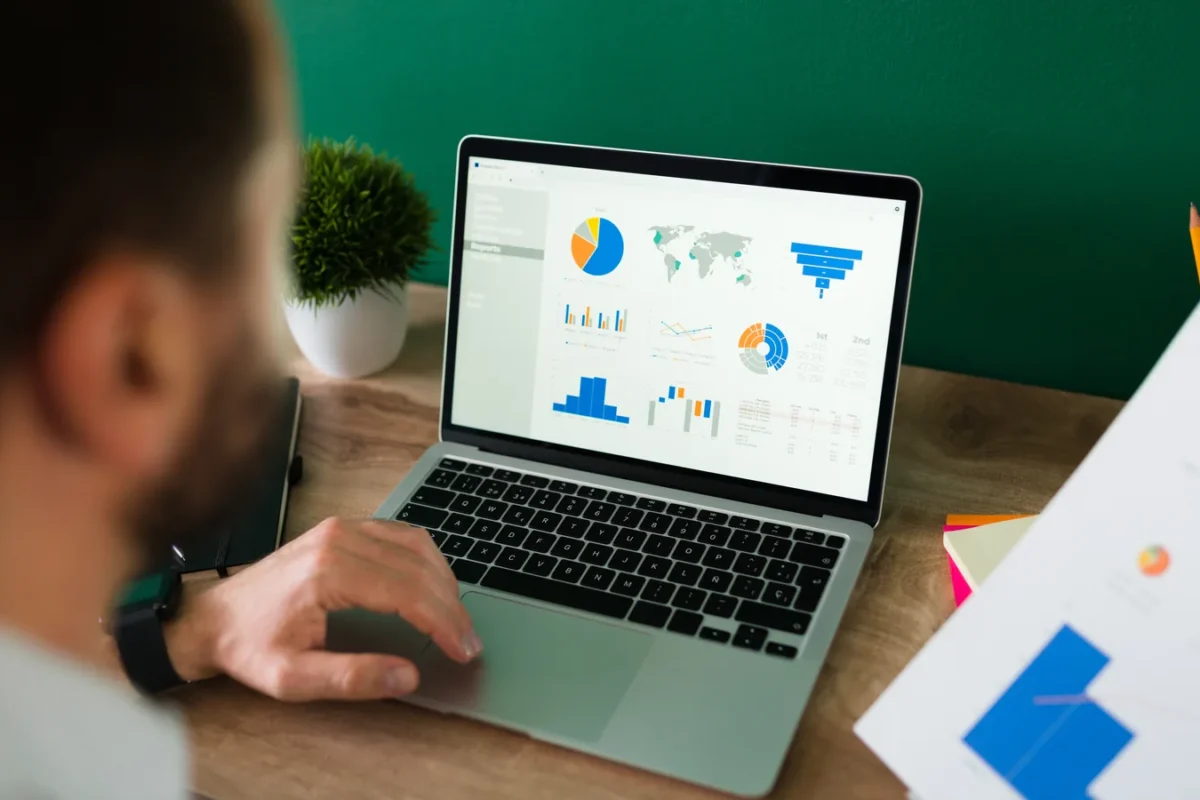 Homme analysant des graphiques de dépenses sur un ordinateur portable, un rapport imprimé à la main