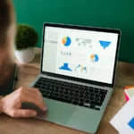 Homme analysant des graphiques de dépenses sur un ordinateur portable, un rapport imprimé à la main