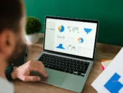 Homme analysant des graphiques de dépenses sur un ordinateur portable, un rapport imprimé à la main
