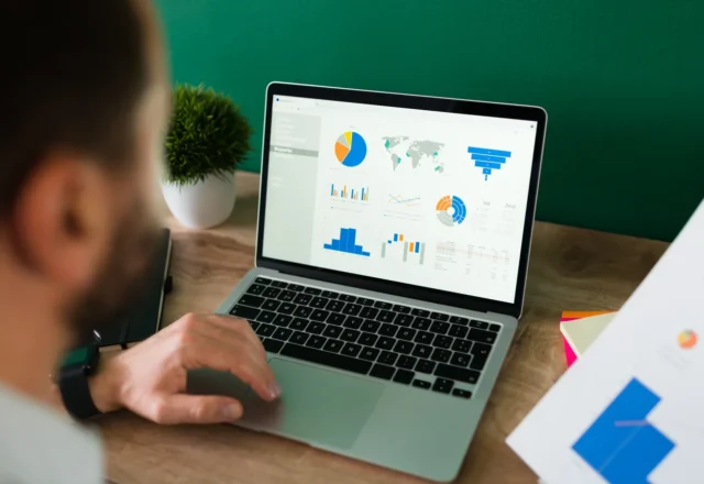 Homme analysant des graphiques de dépenses sur un ordinateur portable, un rapport imprimé à la main
