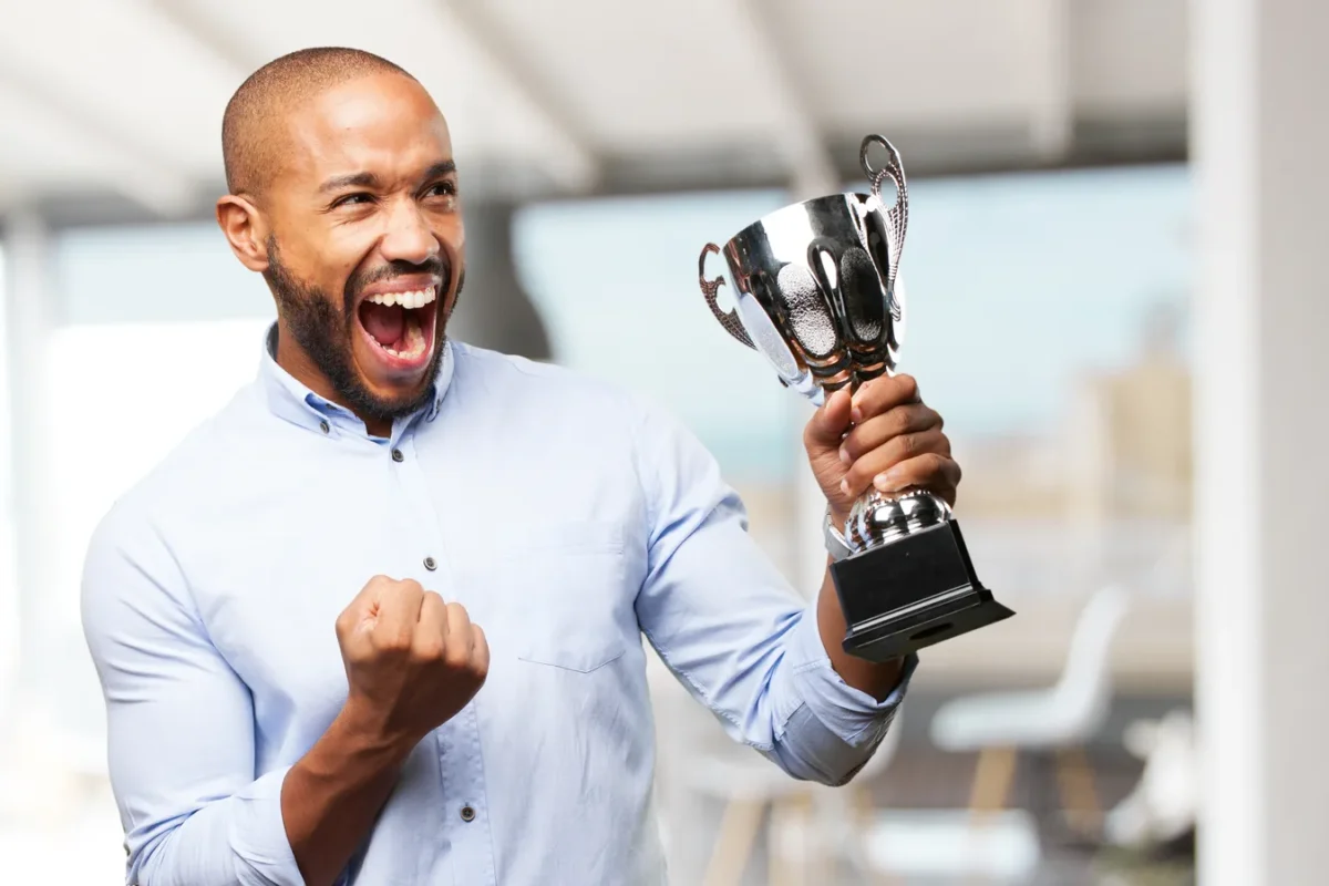 Homme en chemise bleue brandissant un trophée argenté, poing serré en signe de victoire