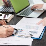 Deux personnes annotent des graphiques et un rapport chiffré devant un ordinateur portable, illustration du chiffrage d’un cas d’usage de l’IA en comptabilité
