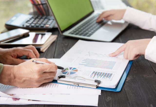 Deux personnes annotent des graphiques et un rapport chiffré devant un ordinateur portable, illustration du chiffrage d’un cas d’usage de l’IA en comptabilité
