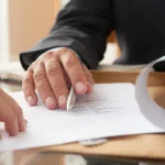 Deux personnes examinent un document imprimé posé sur un bureau, l’une tenant un stylo au-dessus de la page
