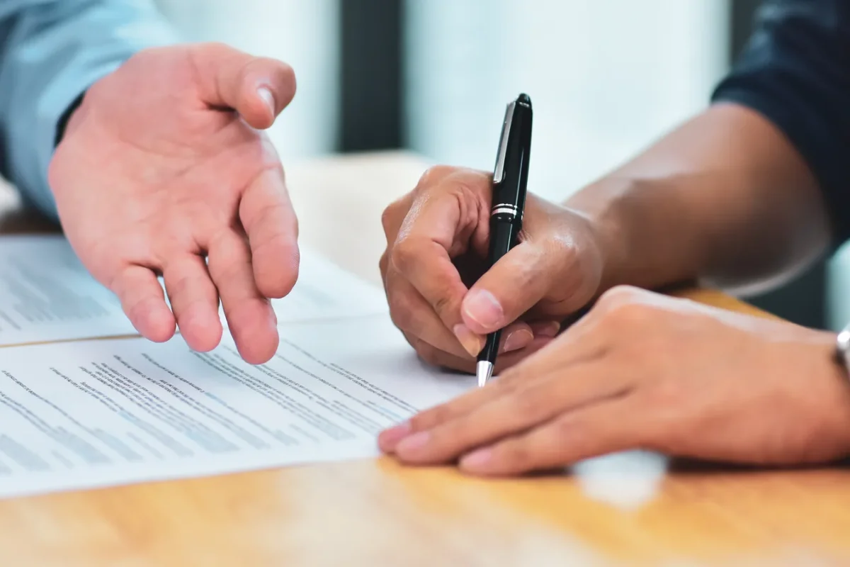 Une main désigne un paragraphe d’un contrat pendant qu’une autre personne le signe au stylo
