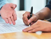 Une main désigne un paragraphe d’un contrat pendant qu’une autre personne le signe au stylo