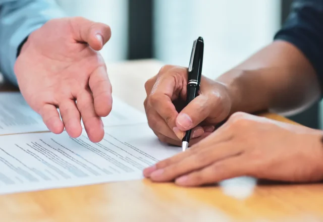 Une main désigne un paragraphe d’un contrat pendant qu’une autre personne le signe au stylo