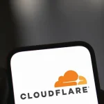 Smartphone affichant le logo Cloudflare tenu en main sur fond sombre