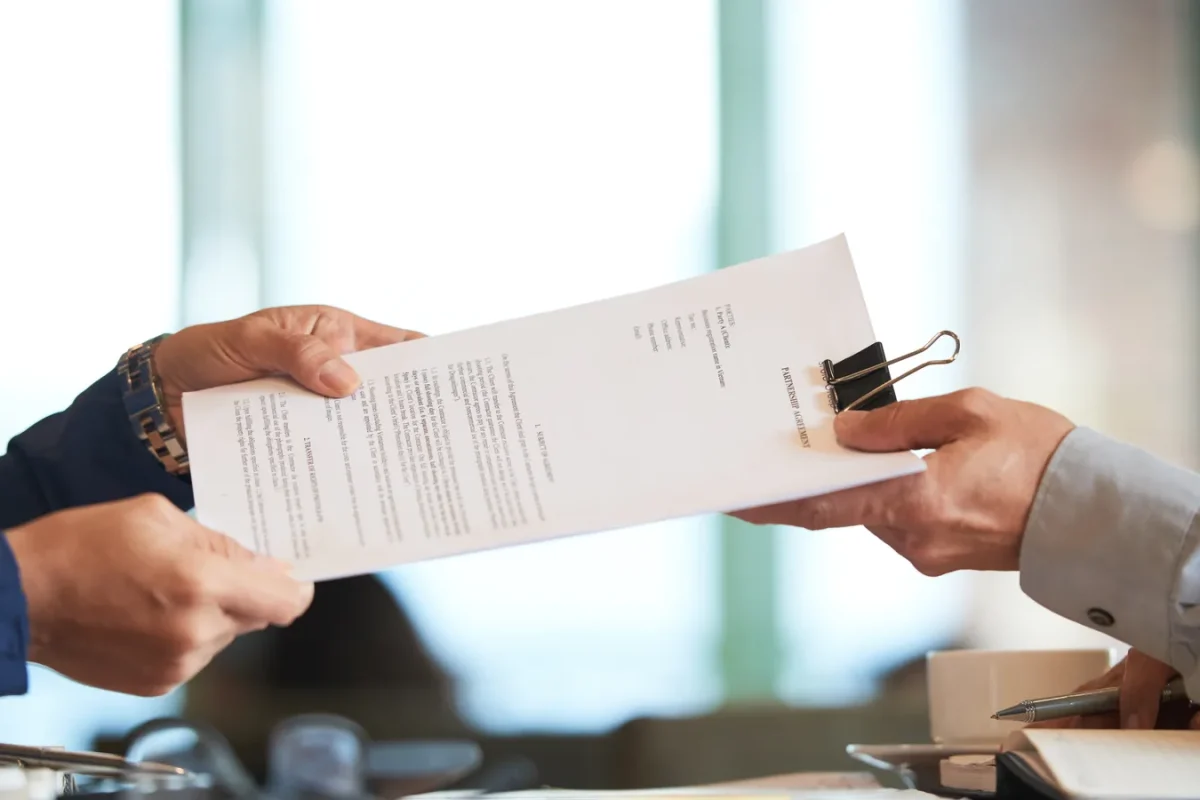 Deux mains se passant un contrat de partenariat imprimé au-dessus d'une table de réunion