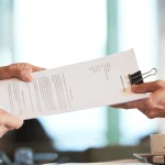 Deux mains se passant un contrat de partenariat imprimé au-dessus d'une table de réunion