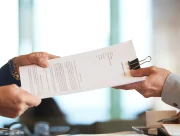 Deux mains se passant un contrat de partenariat imprimé au-dessus d'une table de réunion