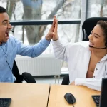 Deux téléconseillers équipés de casques se tapent dans la main devant leurs postes de travail
