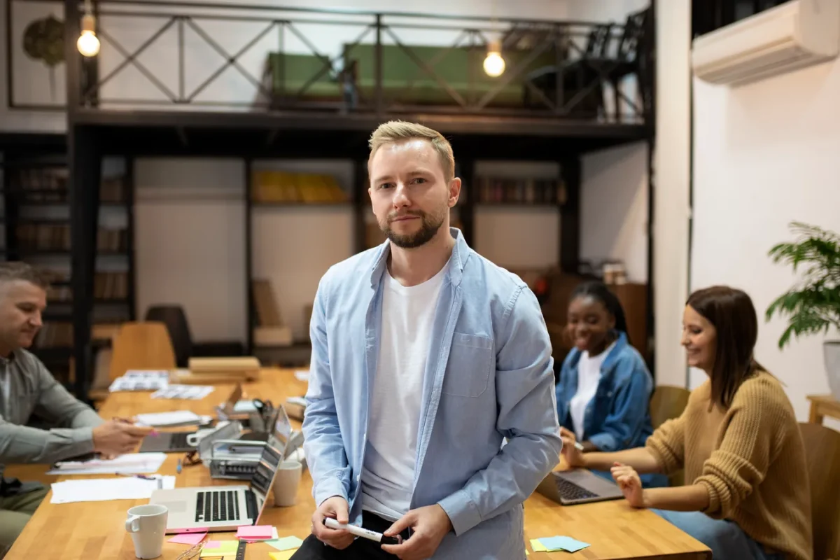 Responsable debout devant une table de réunion où travaille son équipe, un marqueur à la main