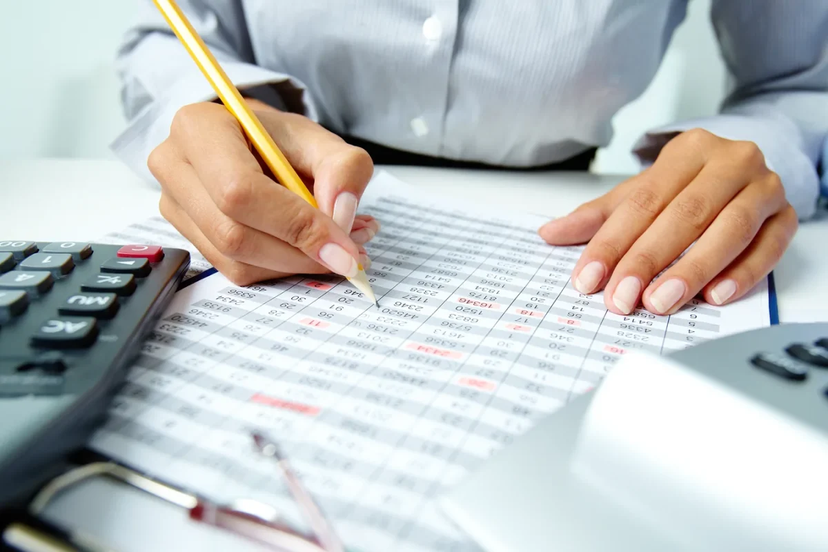 Personne vérifiant au crayon un tableau de chiffres imprimé, à côté de calculatrices