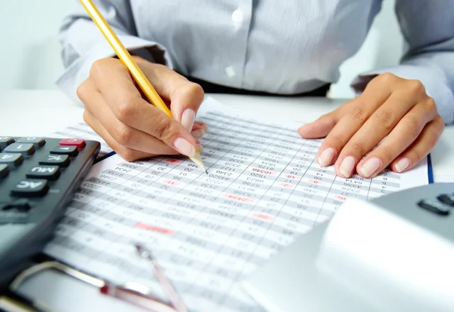 Personne vérifiant au crayon un tableau de chiffres imprimé, à côté de calculatrices