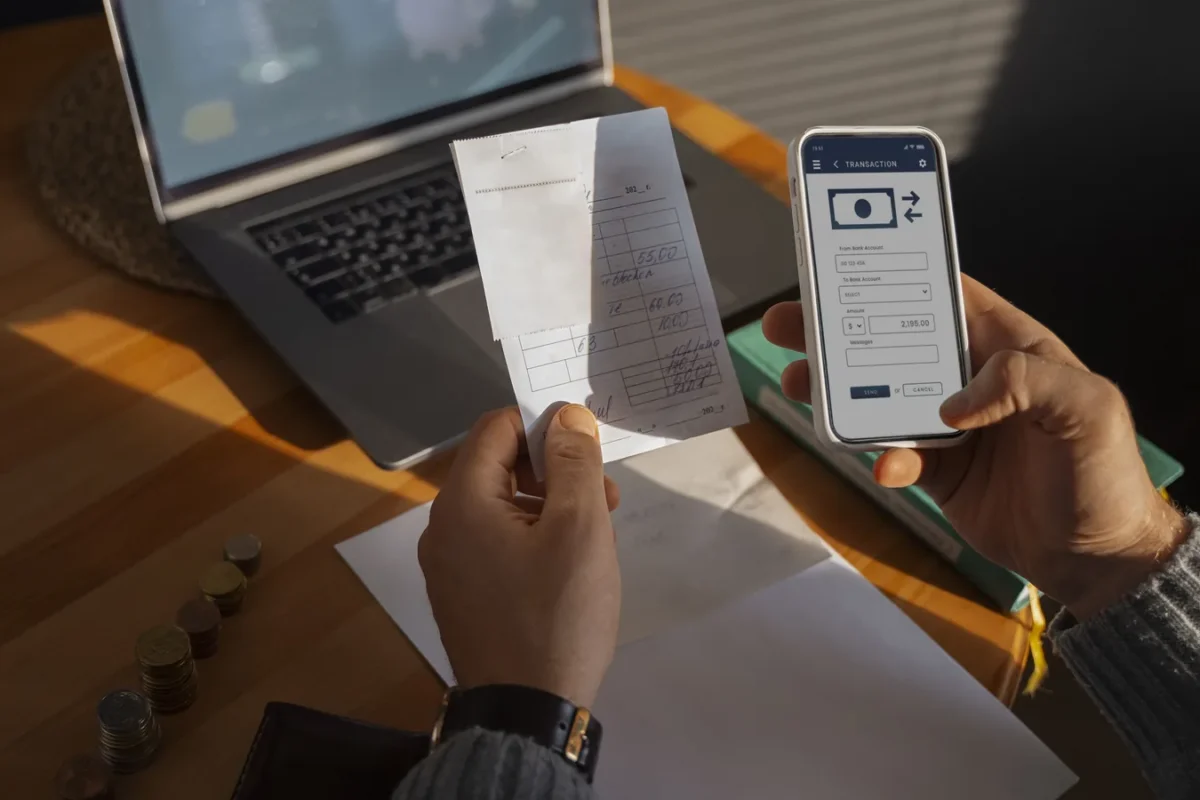 Mains tenant un ticket de caisse et un smartphone affichant une application de virement