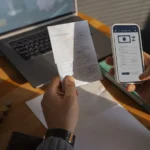 Mains tenant un ticket de caisse et un smartphone affichant une application de virement