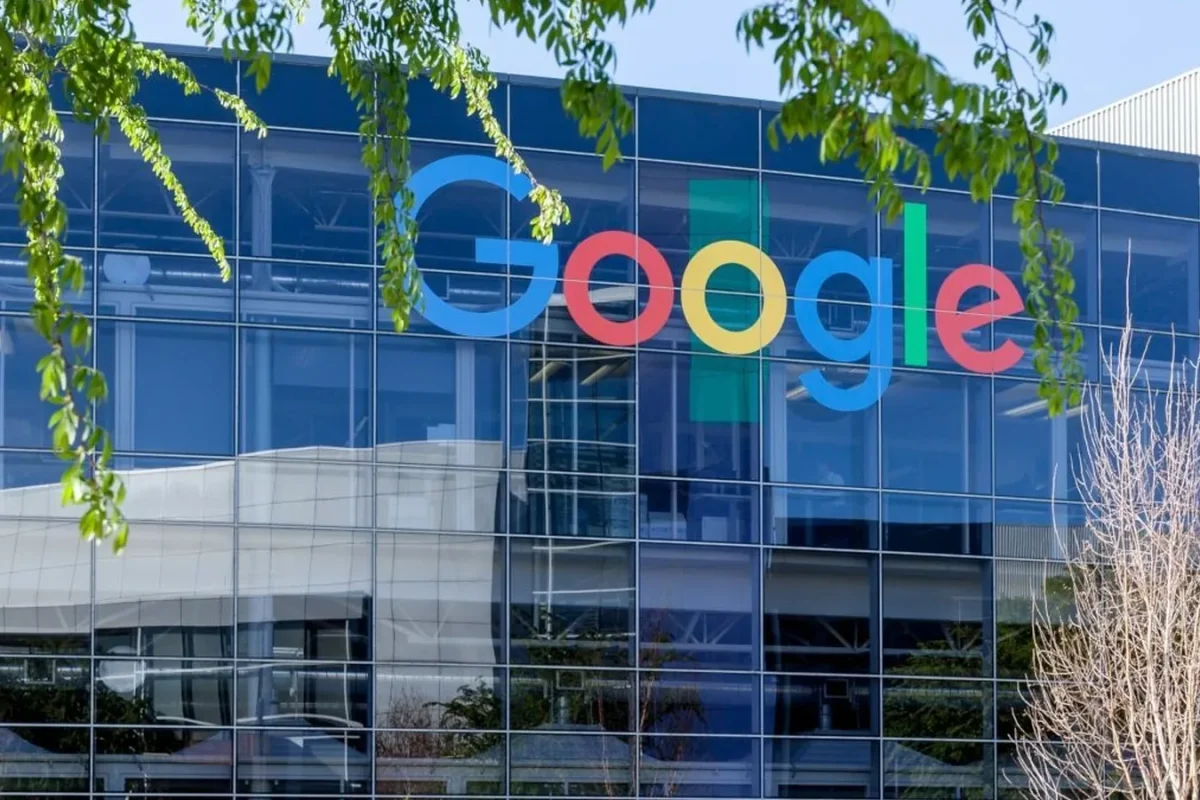 Façade vitrée d’un bâtiment de Google avec le logo de la marque, sous des branches d’arbre
