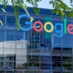 Façade vitrée d’un bâtiment de Google avec le logo de la marque, sous des branches d’arbre