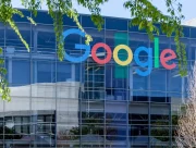 Façade vitrée d’un bâtiment de Google avec le logo de la marque, sous des branches d’arbre