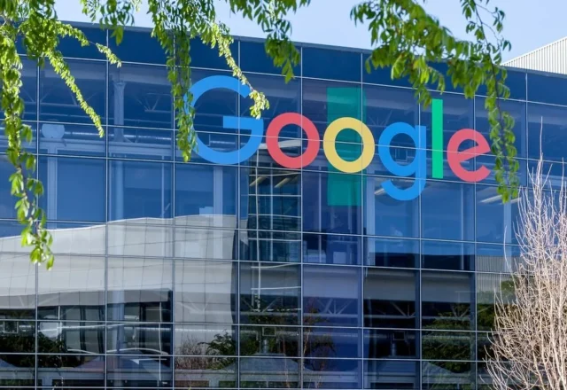 Façade vitrée d’un bâtiment de Google avec le logo de la marque, sous des branches d’arbre
