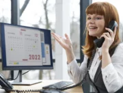 Femme au téléphone devant un écran affichant un calendrier de rendez-vous