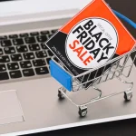 Mini chariot de supermarché contenant une affiche « Black Friday Sale », posé sur le clavier d’un ordinateur portable