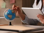 Mains d’une personne faisant tourner un petit globe terrestre tout en consultant une tablette à son bureau