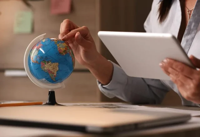 Mains d’une personne faisant tourner un petit globe terrestre tout en consultant une tablette à son bureau