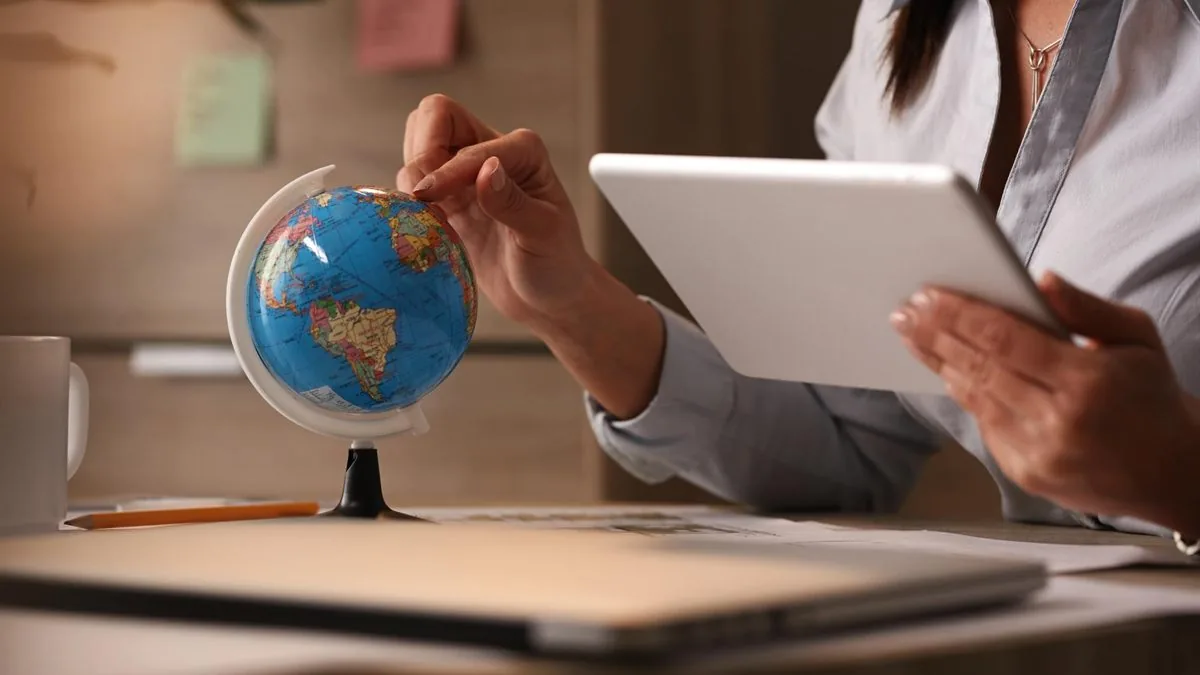 Mains d’une personne faisant tourner un petit globe terrestre tout en consultant une tablette à son bureau