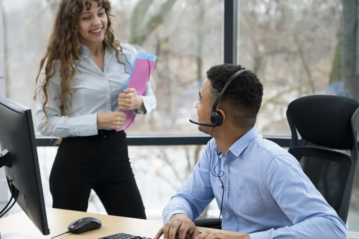 Conseiller en casque à son poste échangeant avec une collègue dans un centre de contacts externalisé
